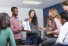 Multi-ethnic group of high school or university students and female teacher at school in classroom. Two students standing up, giving presentation to class. Main focus on the students holding the chart.