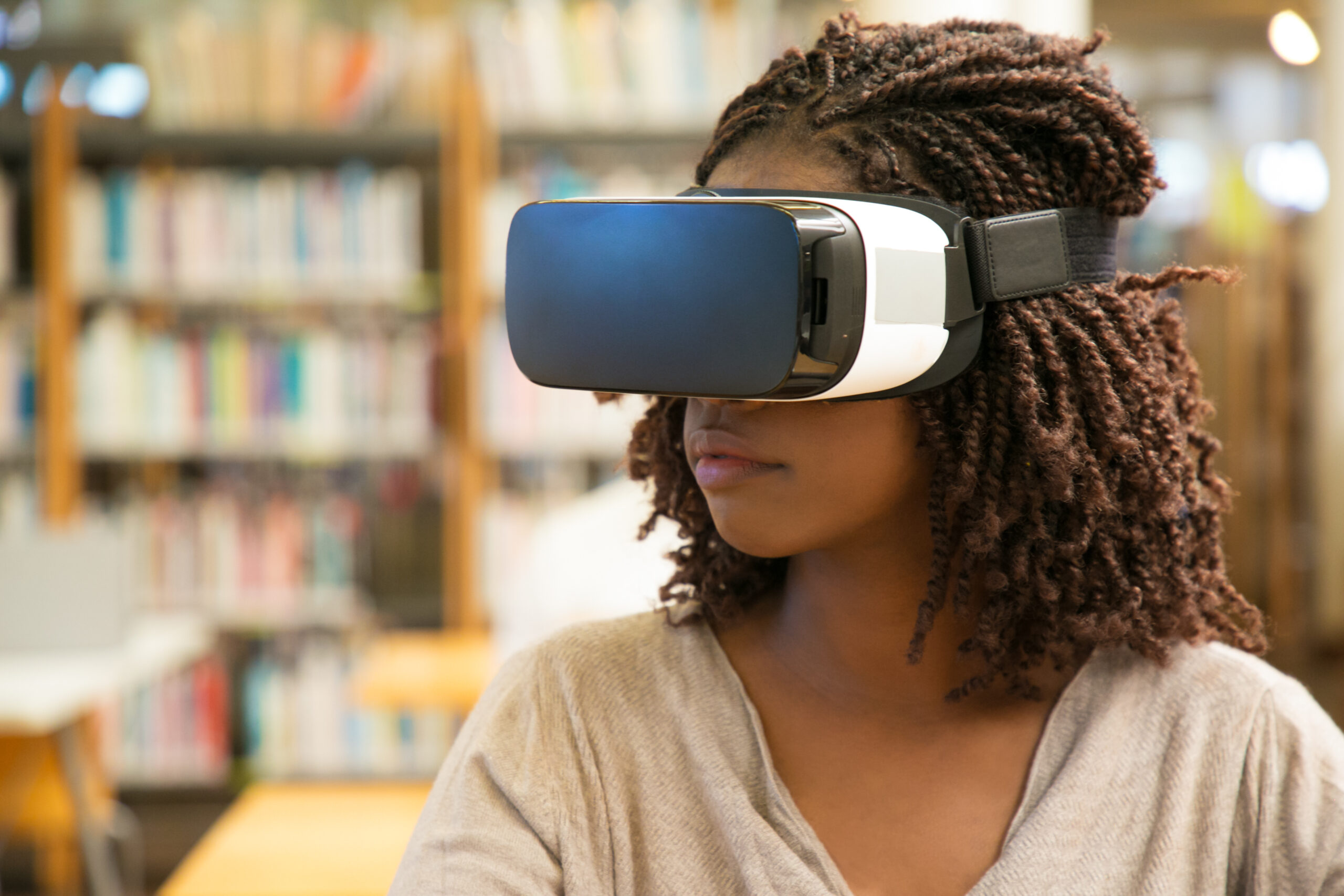 African American student girl using VR glasses for work African American student girl using VR glasses for work in library. Young black woman wearing virtual reality headset, sitting at desk. VR technology concept