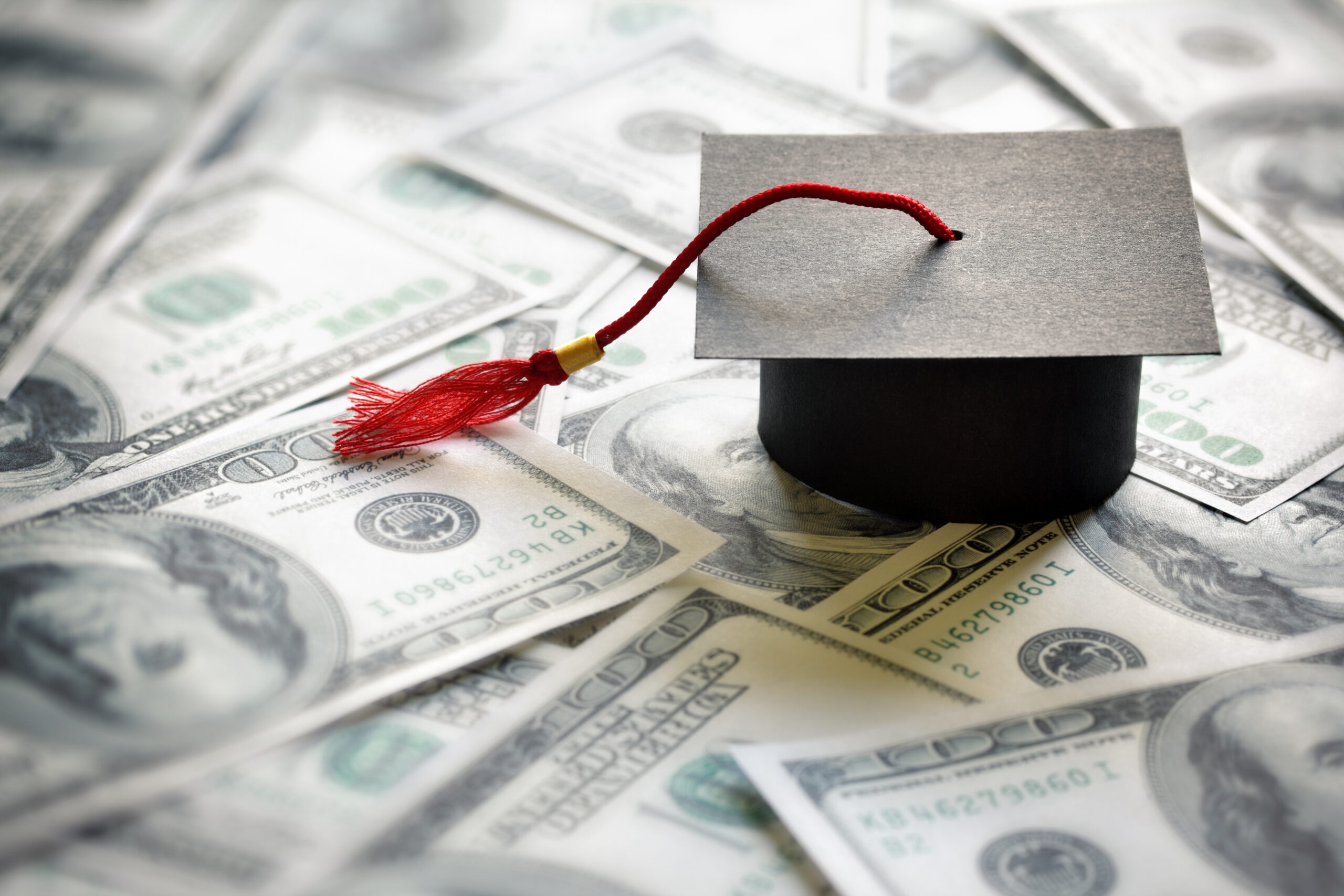 Saving for education Graduation mortar board cap on one hundred dollar bills concept for the cost of a college and university education