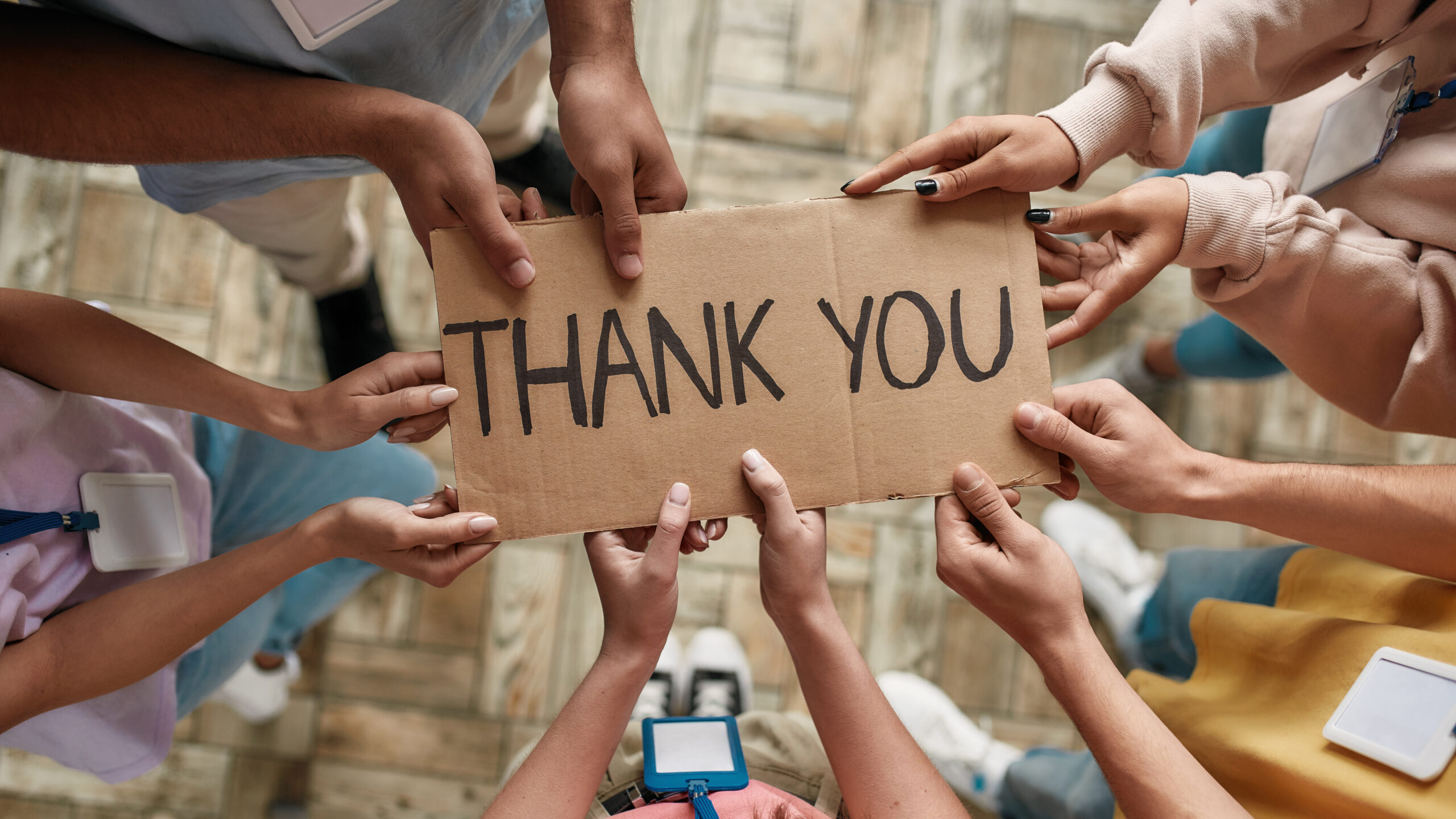 Top view of diverse young volunteers holding card with Thank you lettering while standing in charitable organization office Top view of diverse young volunteers holding card with Thank you lettering while standing in charitable organization office, Selective focus on hands and inscription, Web Banner